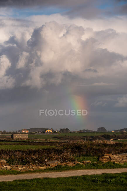 Colorato arcobaleno splendente in mezzo a spesse nuvole dopo la pioggia su un piccolo insediamento in campagna — Foto stock
