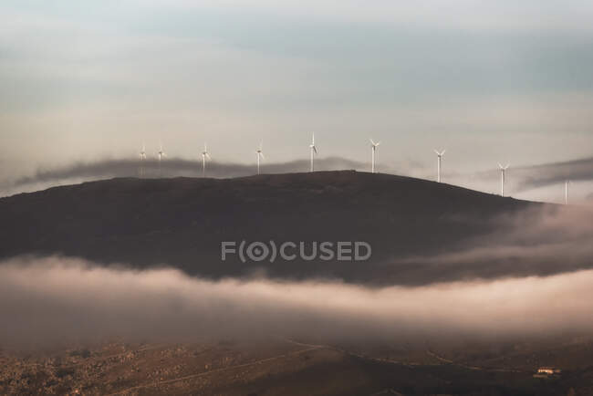 Moinhos de vento da estação eólica moderna localizada na colina na manhã enevoada no campo — Fotografia de Stock