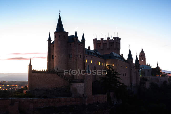 Palácio antigo com janelas brilhantes contra o céu ao pôr-do-sol perto da cidade à noite — Fotografia de Stock