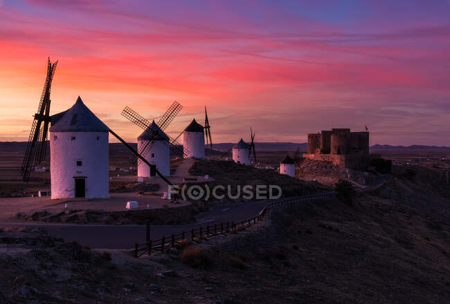 Moinhos de vento antigos e castelo envelhecido contra o céu brilhante do por do sol na noite no campo — Fotografia de Stock