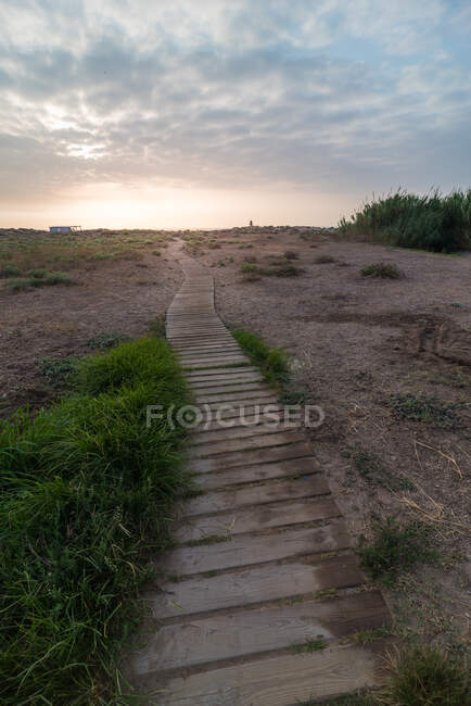Caminho de madeira quebrada passando por um campo calmo contra o céu nublado — Fotografia de Stock