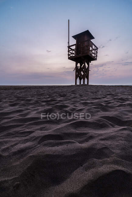 Деревянная башня-спасатель, расположенная на песчаном берегу против закатного неба на курорте — стоковое фото