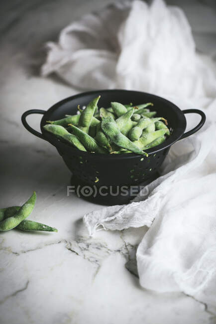 Strainer with uncooked edamames on the table — Stock Photo