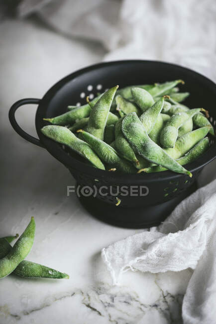 From above black colander with unripe soybeans for edamame dish preparation placed near gauze napkin on marble tabletop — Stock Photo