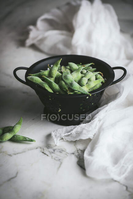 Strainer with uncooked edamames on the table — Stock Photo
