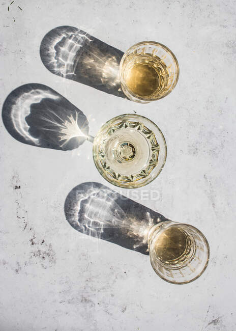 Top view composition of various glasses with alcohol drinks in sunlight leaving shadows and lights on marble surface — Stock Photo