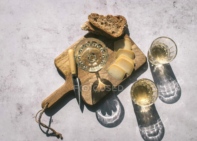 Вид зверху композиція з келихами вина, подається з нарізаним сиром і хлібом з варенням на мармуровому столі з дерев'яною дошкою на сонячному світлі — стокове фото