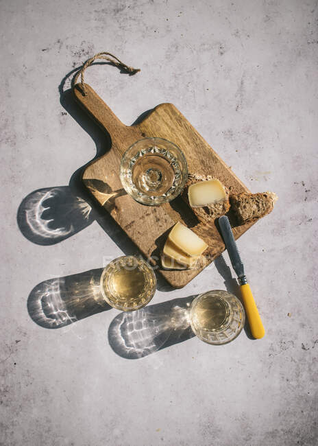 Zusammensetzung von oben mit Weingläsern, serviert mit Scheibenkäse und Brot mit Marmelade auf Marmortisch mit Holzbrett im Sonnenlicht — Stockfoto