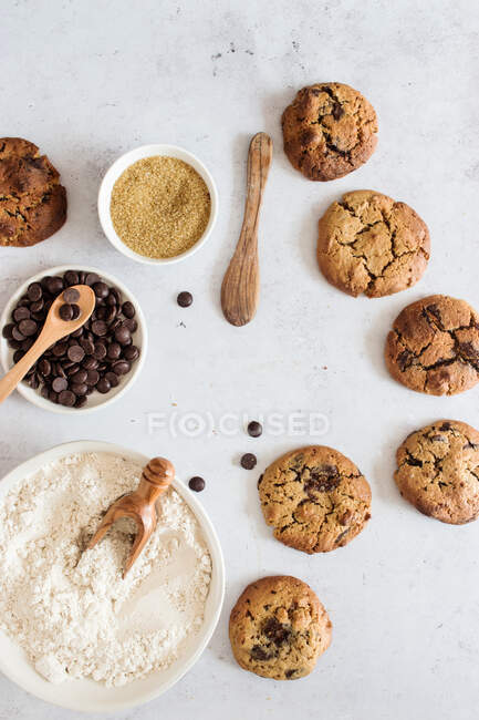Вид зверху композиція печива ручної роботи з шоколадними чіпсами, розміщеними на мармуровому столі з інгредієнтами для рецепту — стокове фото