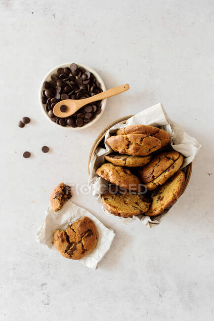 Vista superior de deliciosas galletas dulces caseras en un tazón colocado en una mesa de mármol cerca de la olla con chips de chocolate - foto de stock
