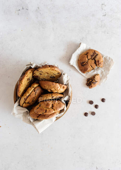 Vista dall'alto di deliziosi biscotti dolci fatti in casa in ciotola posizionati sul tavolo di marmo vicino alla pentola con gocce di cioccolato — Foto stock