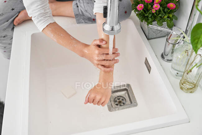 Проколотий образ дитини, яка миє руки в кухонній раковині, щоб запобігти інфекції. — стокове фото