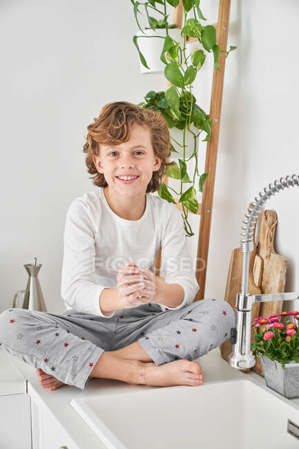 Niño rubio lavándose las manos en el fregadero de la cocina para prevenir cualquier infección - foto de stock