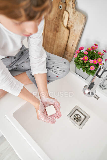 Niño rubio lavándose las manos en el fregadero de la cocina para prevenir cualquier infección - foto de stock