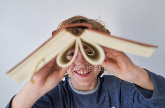 Blond boy in pajamas using a book as binoculars — Stock Photo