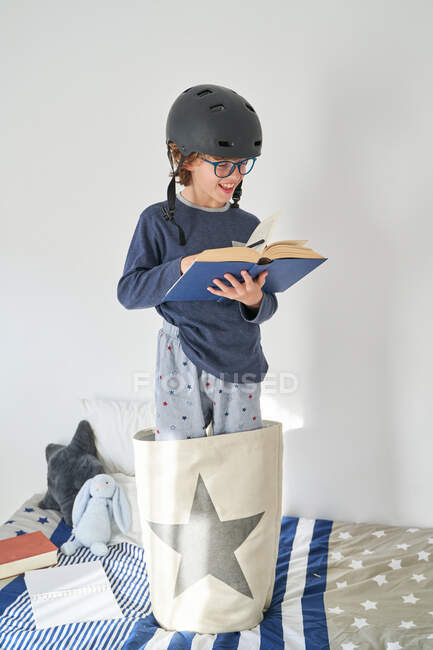 Niño rubio en pijama con casco y libro de investigación - foto de stock