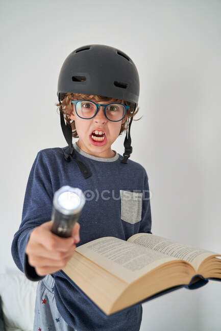 Blond gamin en pyjama avec un casque une lampe de poche et un livre de recherche — Photo de stock