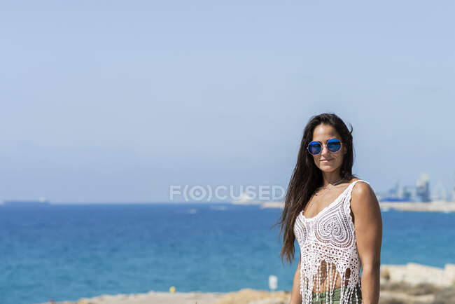 Усміхнена молода жінка в сонцезахисних окулярах на пляжі — стокове фото