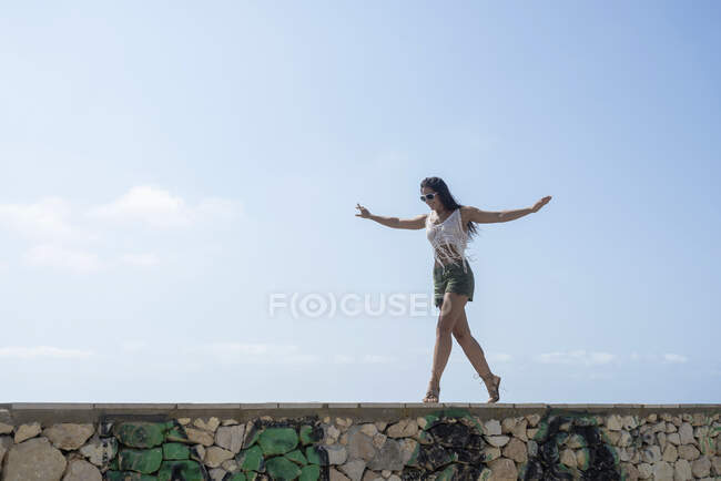 Ritratto a figura intera di donna bruna spensierata in pantaloncini che danza su un muro contro il mare — Foto stock