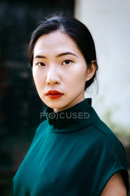 Young asian woman in trendy dress on in green bushes and looking at camera in aged garden — Stock Photo