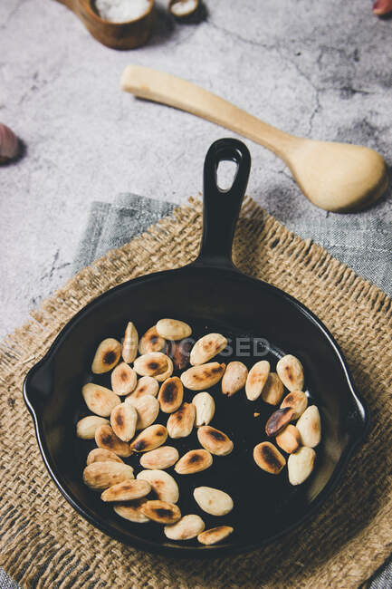 From above tasty roasted almond nuts on black metal pan on burlap napkin in composition with wooden spoon on gray rustic table — Stock Photo