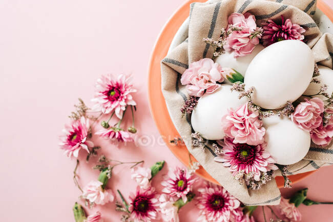Vista superior del ramo de flores delicadas dispuestas cerca del plato con huevos de pollo en el día de Pascua sobre fondo rosa - foto de stock