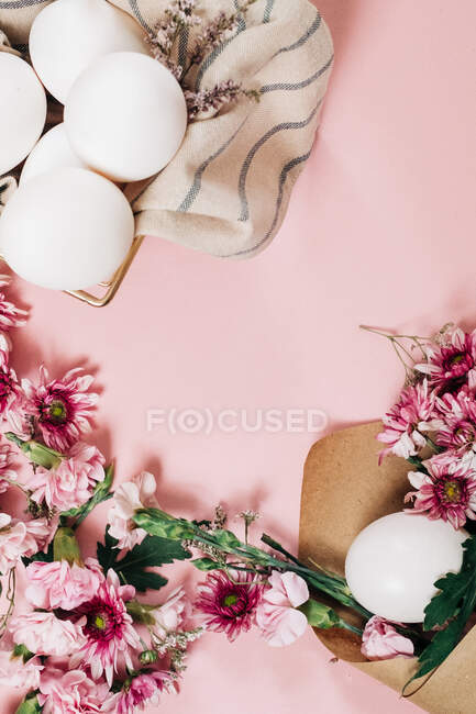 From above bunch of delicate flowers arranged near plate with chicken eggs on Easter Day on pink background — Stock Photo