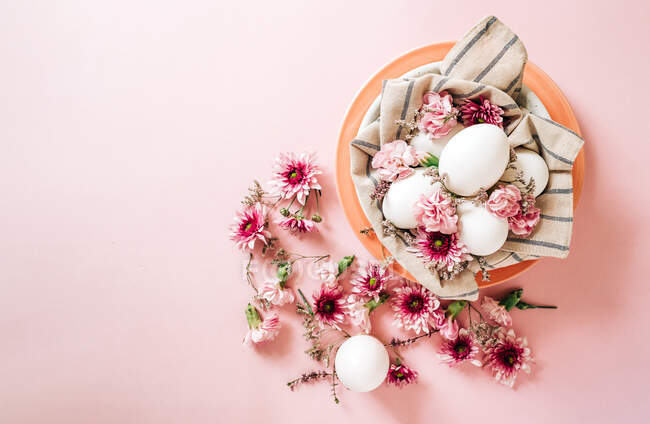 Vista superior de um monte de flores delicadas dispostas perto da placa com ovos de galinha no dia de Páscoa no fundo rosa — Fotografia de Stock