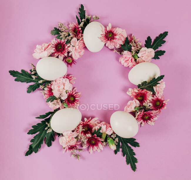De arriba elegante corona de Pascua hecha de flores y huevos de pollo y colocada sobre fondo rosa - foto de stock
