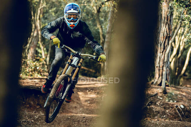 Unrecognizable man looking at camera in helmet, gloves and protection glasses jumping doing whip trick downhill during mountain biking practice in wood forest — Stock Photo