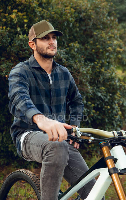 Mountain biking sportsman without protection sitting on bike in the middle of a forest looking away — Stock Photo