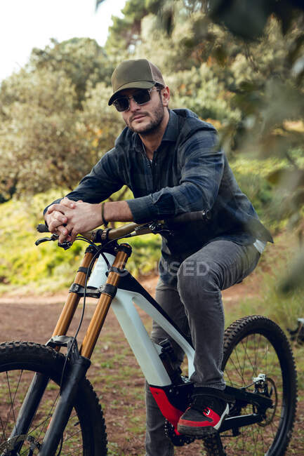Bicicleta de montaña deportista sin protección sentado en bicicleta en medio de un bosque mirando a la cámara - foto de stock