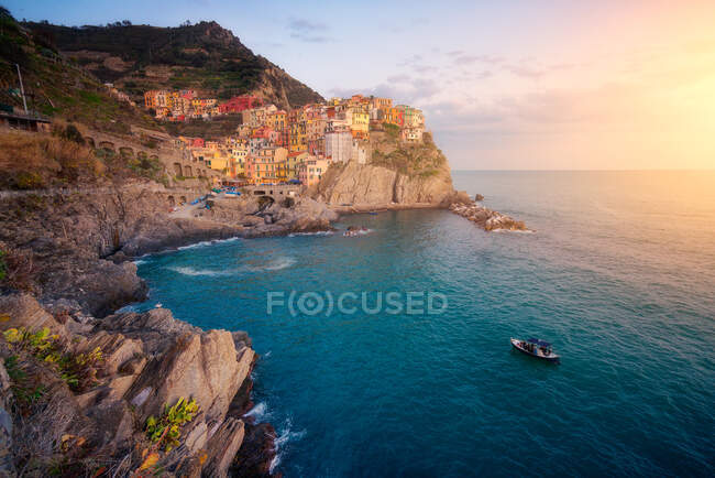 Cenário maravilhoso com pequena cidade colorida na costa rochosa lavagem pela água do oceano calma durante o pôr do sol — Fotografia de Stock