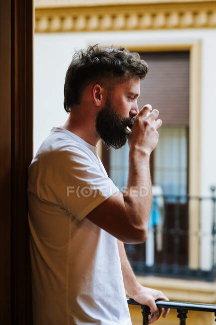 Бородатый парень с горячим напитком отдыхает на балконе — стоковое фото