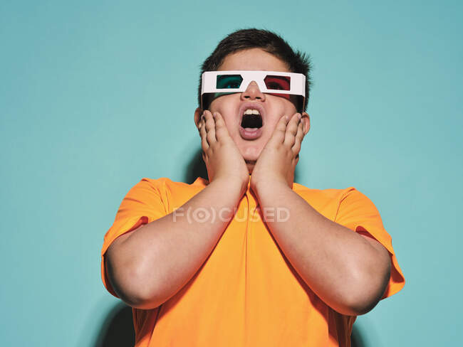 Schockiert überrascht preteen boy mit geöffnetem Mund in einer speziellen Brille mit stereoskopischer blauer und roter Linse schauen weg und genießen 3D-Grafik-Video vor türkisfarbenem Hintergrund in modernen Studio — Stockfoto