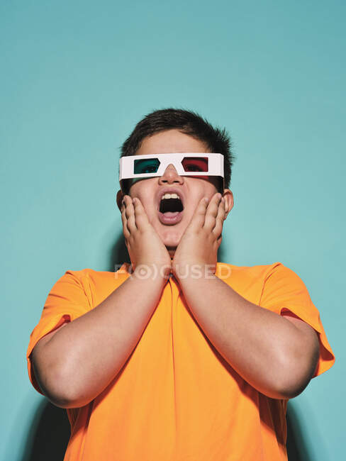 Шокований здивований хлопчик з ротом відкрився в спеціальних окулярах зі стереоскопічною синьою і червоною лінзою, дивлячись і насолоджуючись 3d графічним відео на тлі бірюзового фону в сучасній студії — стокове фото