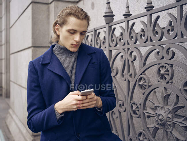 Elegante joven navegando en el teléfono inteligente en la calle en la calle de la ciudad - foto de stock