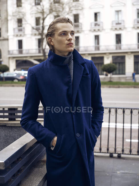 Seitenansicht von stilvollen jungen Mann mit trendiger Frisur gekleidet in elegantem Mantel steht vor grauer Steinmauer in der Stadt — Stockfoto