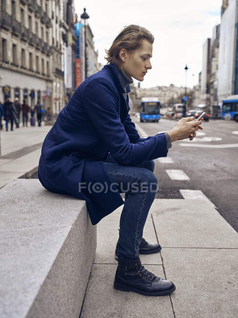 Vista laterale del giovane bel maschio in abito elegante guardando smartphone — Foto stock