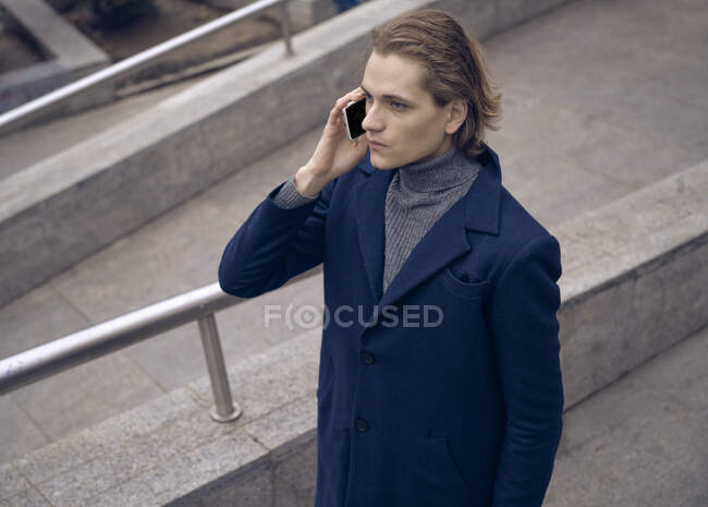 From above of serious young businessman in elegant coat checking message on mobile phone while standing on stone staircase on city street — Stock Photo