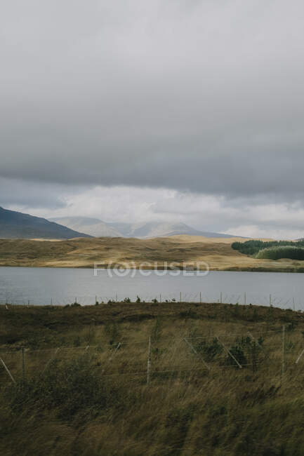 Мрачные шотландские пейзажи с спокойным озером под серым облачным небом в высокогорье осенью — стоковое фото