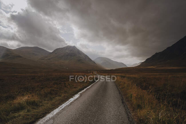 Estrecha carretera de asfalto que pasa por colinas cubiertas de hierba montaña en día nublado en la naturaleza - foto de stock