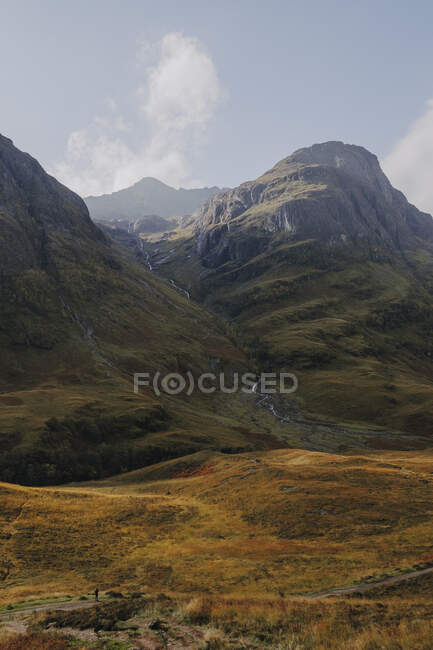 Tranquil scenery of Scottish countryside with yellow grassland in rocky mountain against cloudy sky — Stock Photo