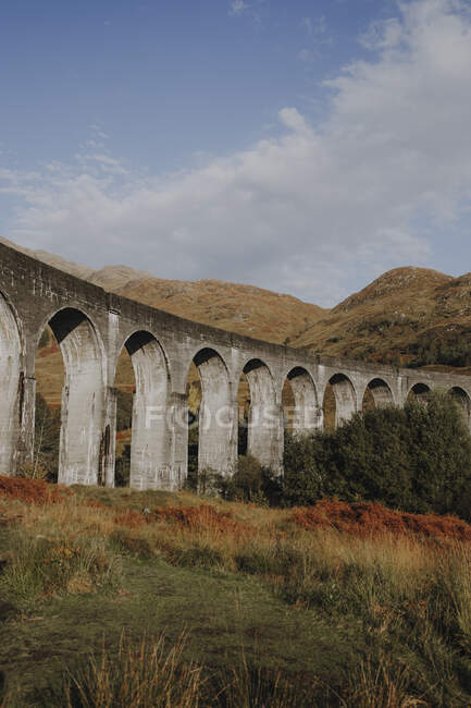 Low angle of old railway viaduct in Scottish highland against mountains and blue cloudy sky in autumn day — Stock Photo