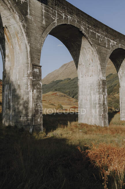 Низький кут старої залізничної віадука в шотландському високогір'ї проти гір і блакитного хмарного неба восени. — стокове фото