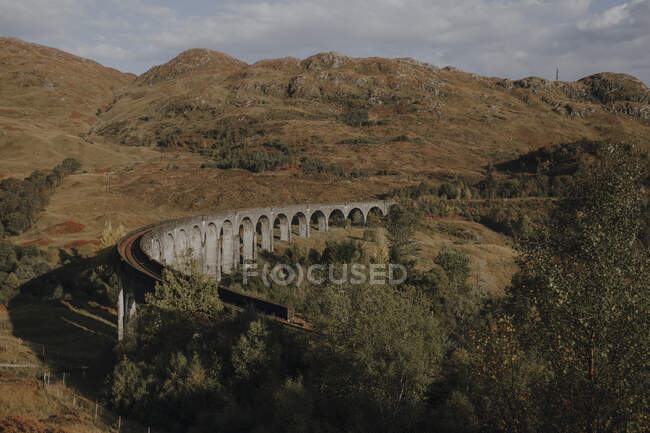 Desde arriba viejo viaducto ferroviario en las tierras altas escocesas contra las montañas y el cielo azul nublado en el día de otoño - foto de stock