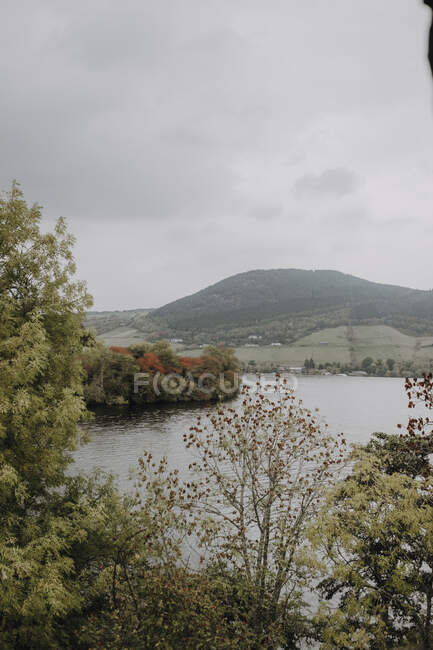 Bela paisagem tranquila de lago cercado por floresta verde e montanhas nebulosas no dia de outono nublado na Escócia — Fotografia de Stock