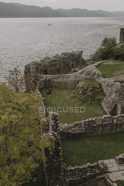 From above of stone walls of ancient castle located on green hill near lake with foggy mountains in background in Scottish countryside — Stock Photo