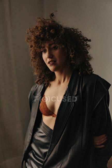 Femme sensuelle en veste et soutien-gorge en cuir avec des cheveux bouclés dans la chambre — Photo de stock