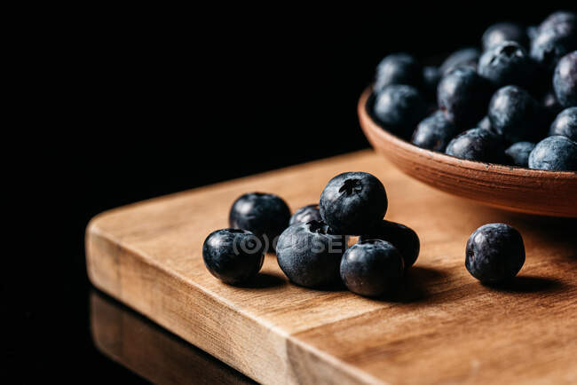 Bleuet mûr frais placé sur une table en bois près d'un bol avec des baies sur fond noir — Photo de stock